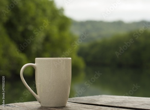 coffee cup / A white cup of coffee is placed on the floor of an old wooden table with a natural backdrop and a blur.