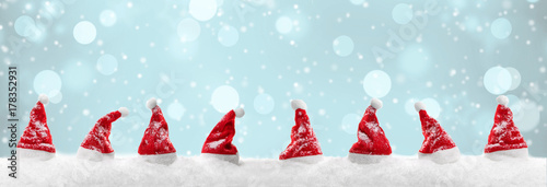 Rote Weihnachtsmützen im Schnee mit winterlichem Bokeh im Hintergrund