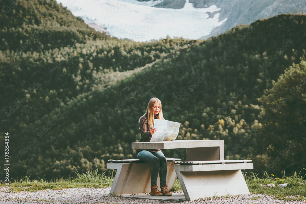 Fototapeta premium Young Woman holding map planning journey route in Norway sitting at the table Travel Lifestyle concept adventure vacations outdoor