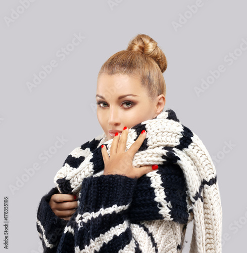 Winter portrait of a beautiful woman wearing sweater and scarf posing against blue background.