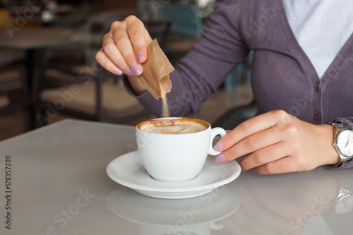 Young woman adding sugar in coffee