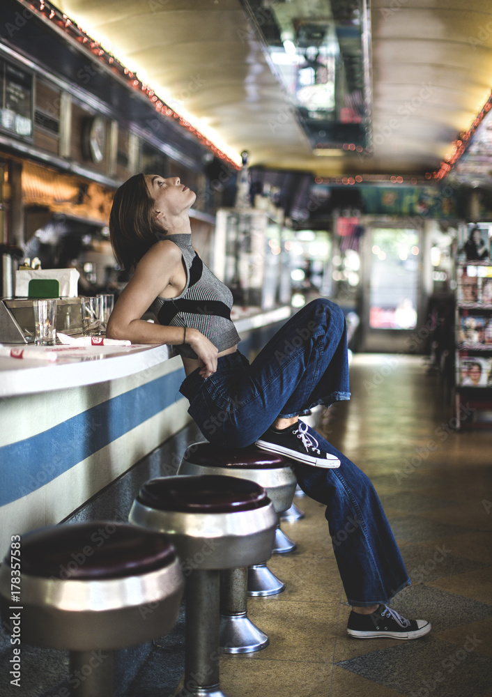 Side view of woman wearing jeans and sleeveless top leaning against a bar  counter in a restaurant, looking up. Stock Photo | Adobe Stock