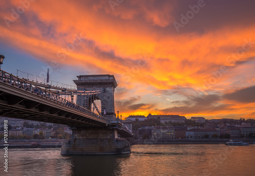 Budapest, Hungary - Dramatic orange sunset with beautiful clouds, Szechenyi Chain Bridge and sightseeing boats on River Danube