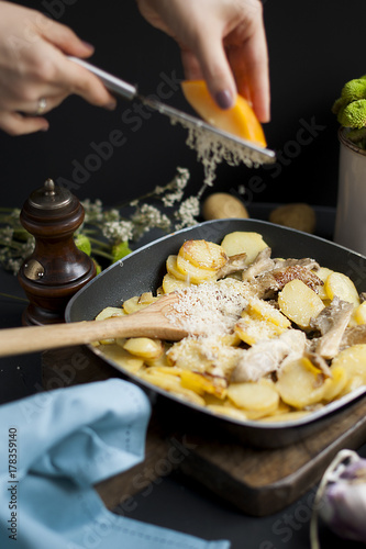 fried potatoes with mushrooms and cheese, in a frying pan, on a black background