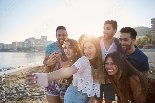 Happy girl taking selfie with friends on beach