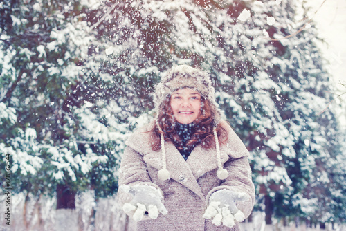 Happy girl in winter clothes throwing snow in the air in winter holidays.