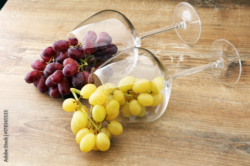 Wineglasses with white grapes and red grapes on wooden background.