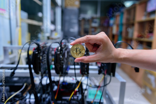 man's hand holding golden Bitcoin on Bitcoin mining background