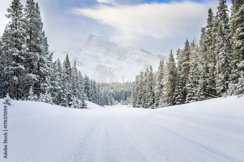 Snow Covered Road in a Forested Mountain Landscape in Winter. Dangerous Driving Conditions.