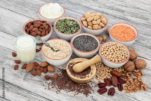 Vegan health food with soya beans, seeds, nuts, soya milk, yoghurt and chunks. Foods high in fibre, antioxidants, vitamins and minerals. On rustic wood background.