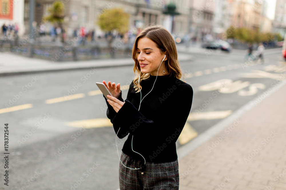 Young brunette woman using mobile while standing on street and  waiting for a bus or taxi