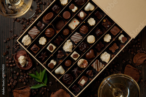 Chocolate pralines box on a wood table with two glasses of white wine and mint and coffee beans. Romantic sweet dinner in two.