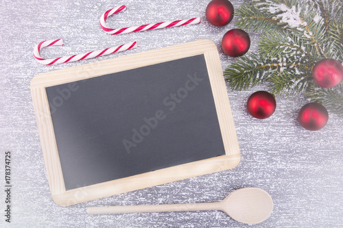 Christmas cooking utensils and a snowy tree on a stone table. Top view with board for copying text for text