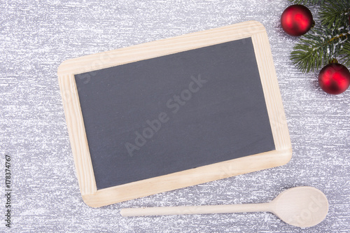 Christmas cooking utensils and a snowy tree on a stone table. Top view with board for copying text for text