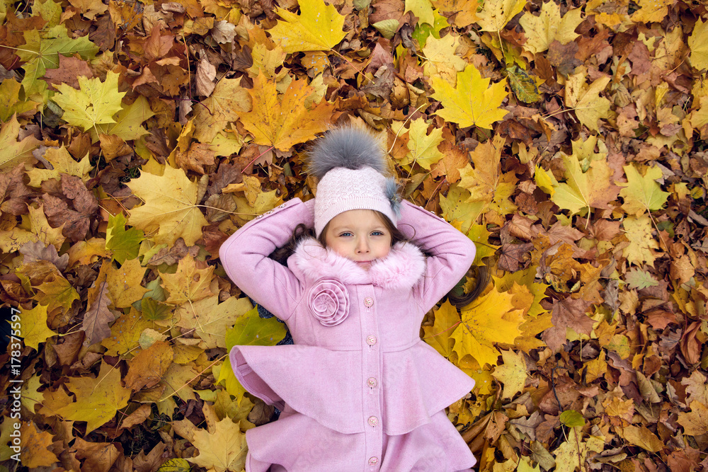 baby girl lying on autumn leaves in pink coat
