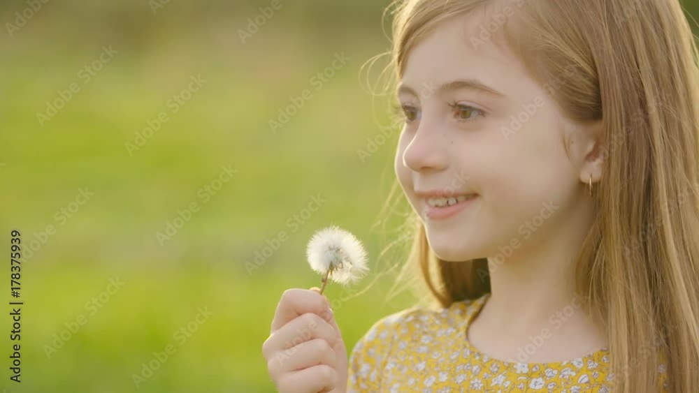 Young Girl Profile Blowing Dandelion Slow Motion. close up profile view of a young girl is grass meadow blowing on a dandelion flower in slow motion and smiling
