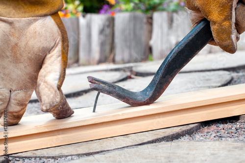man's hands using a crowbar to remove a nail from a wooden plank