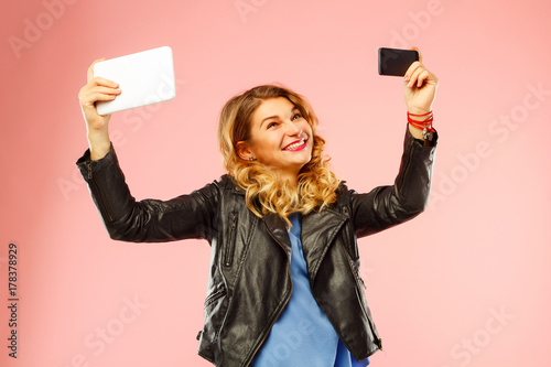 Portrait of a beautiful young woman making selfie both on smart phone and tablet at the same time. Happy young woman photographing herself. photo