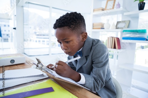 Fotografie Boy imiting as businessman writing on paper attached to