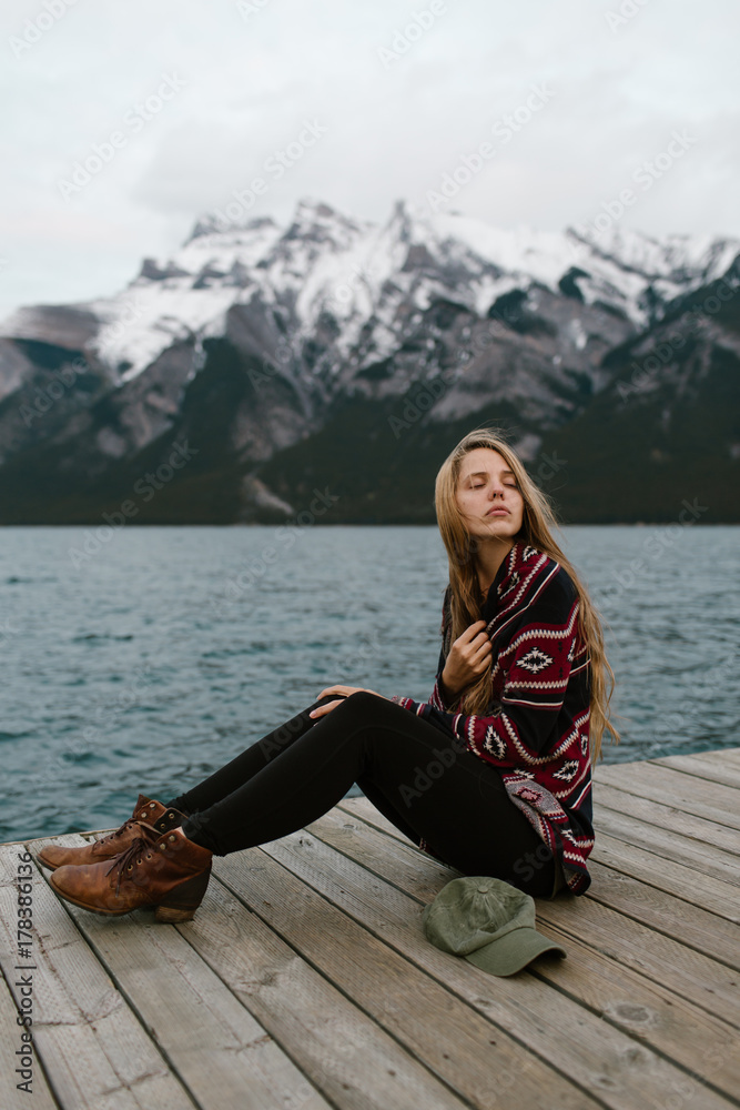 Sad Young Woman with Long Hair Resting on the Mountain Lake Dock