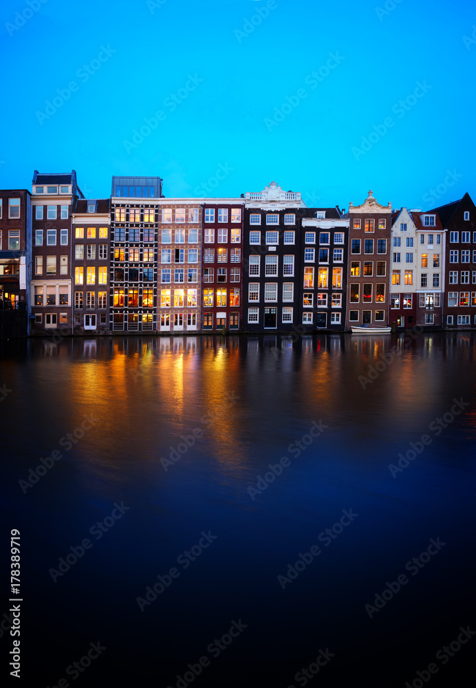 Houses facades over canal with reflections illuminated at blue night, Amsterdam, Netherlands, retro toned