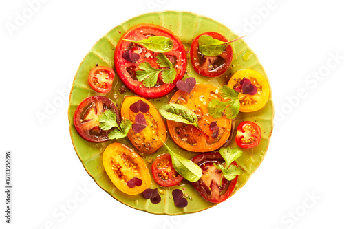 Green plate of salad with sliced tomatoes on white