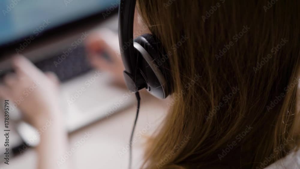 Crop woman working as office assistant using laptop and headphones