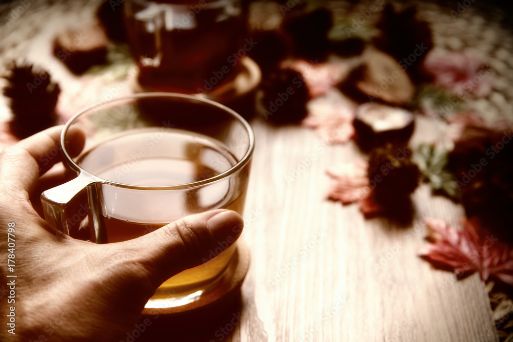 Female hands holding cup of tea from rose hip tea and bouquet of rose hips and chestnuts, autumn leaves on the wooden background.Seasonal, vitamin drink.Autumn background. Female hands holding cup of tea from rose hip tea and bouquet of rose hips and chestnuts, autumn leaves on the wooden background.Seasonal, vitamin drink.Autumn background.