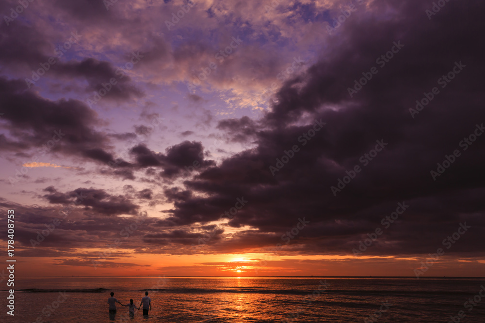 Silhouette of family members join hands to play in the sea at sunset with sun shines on the surface of the sea