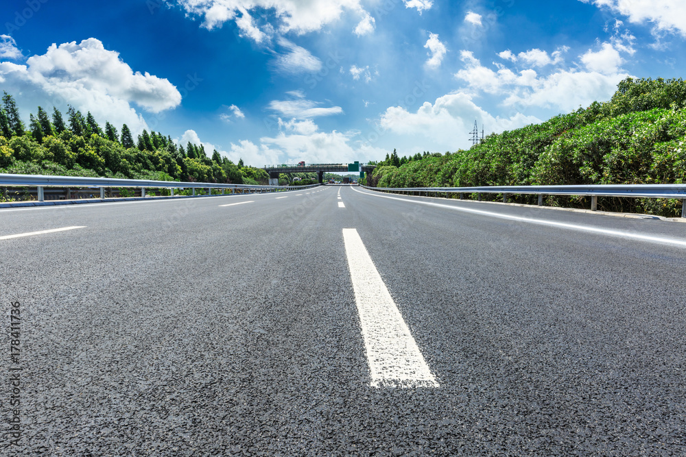asphalt road and green forest under the blue sky