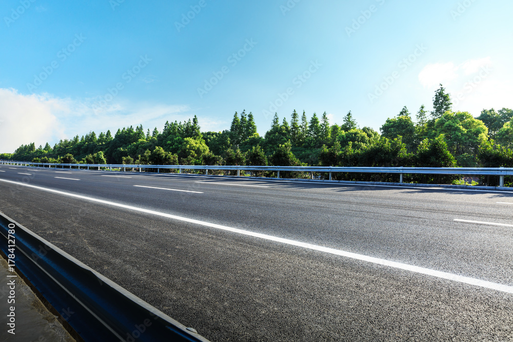 Fototapeta premium asphalt road and green forest under the blue sky