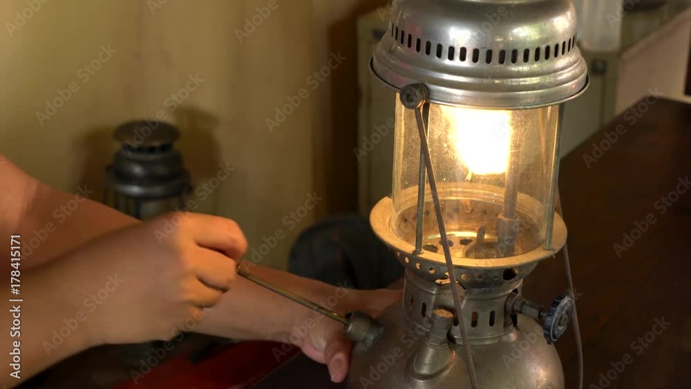 Asian man using pump handle to light a pressurized kerosene lantern. Vintage oil lamp antique hurricane lamp.