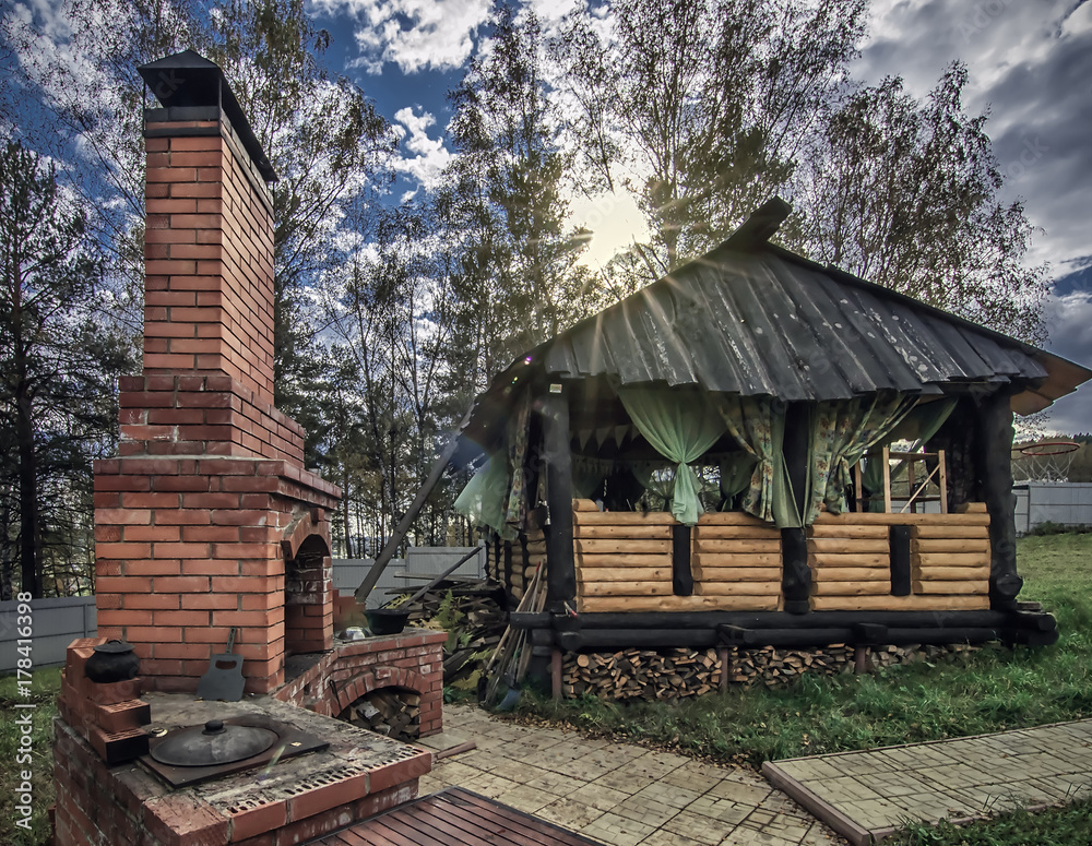 landscape of sunny day with wooden gazebo and outdoor brick oven in backyard