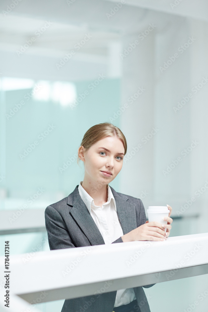 Waist-up portrait of attractive young manager in formalwear posing for photography while enjoying fragrant coffee at spacious office lobby Waist-up portrait of attractive young manager in formalwear posing for photography while enjoying fragrant coffee at spacious office lobby