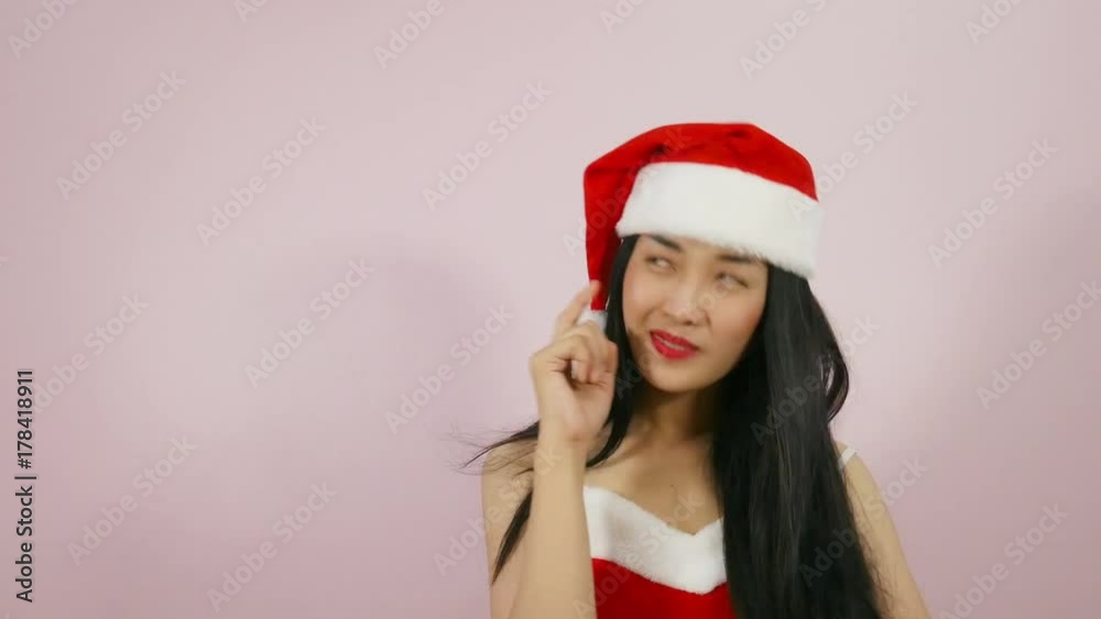 Beautiful thinking woman have an idea in santa claus christmas costume holding finger and looking up on pink background Beautiful thinking woman have an idea in santa claus christmas costume holding finger and looking up on pink background