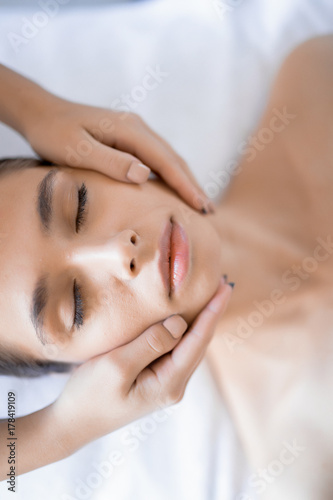 Relaxed young woman having her face massaged in day spa salon