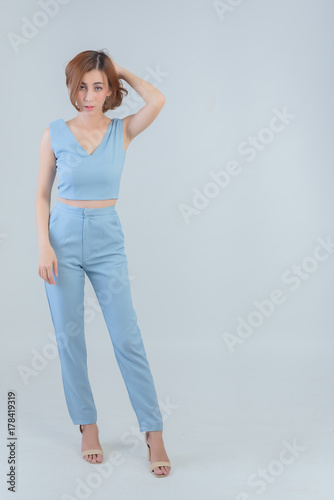 Full length portrait, Smiling young woman in blue shirt and blue long pants standing on a white background. Free from copy space. © vipubadee