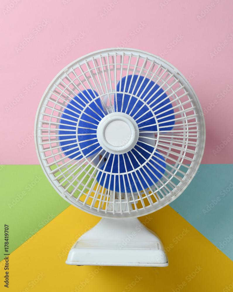 White plastic fan with blue louvres on a multicolored pastel background. Top view.