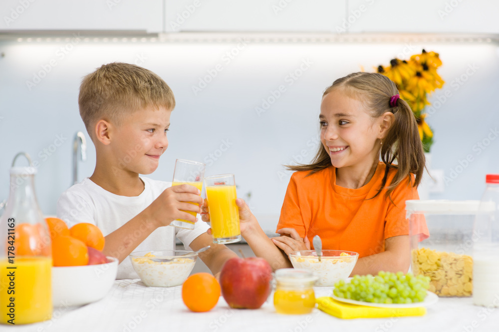 Happy children clink glasses with orange juice at breakfast Happy children clink glasses with orange juice at breakfast
