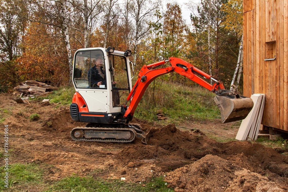 Obraz premium Mini excavator on construction site. Excavator regulates the terrain around the house.