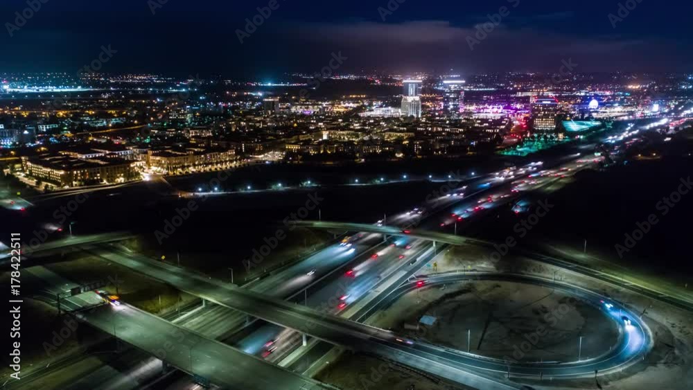 Urban aerial drone time lapse in motion or hyperlapse at night flying towards a highway with cars and traffic showing the on and off ramp circles indicative of the fast paced futuristic city lifestyle