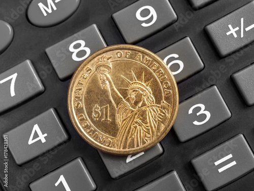 US one dollar coin on the calculator. Close up.