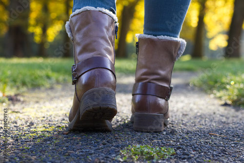 Woman with leather shoes walks on a footpath in autumn park, low angle from behind.