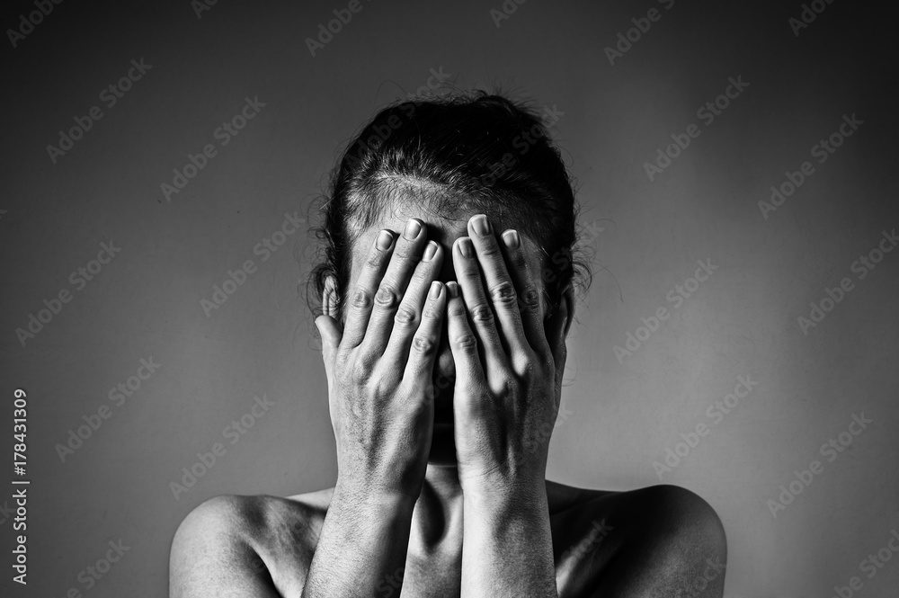 Concept of fear, shame, domestic violence. Woman covers her face her hands on light scratched background. Black and white image. Concept of fear, shame, domestic violence. Woman covers her face her hands on light scratched background. Black and white image.