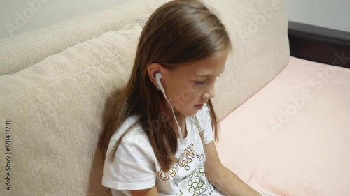 little girl with headphones listening to music sitting on the couch. photo