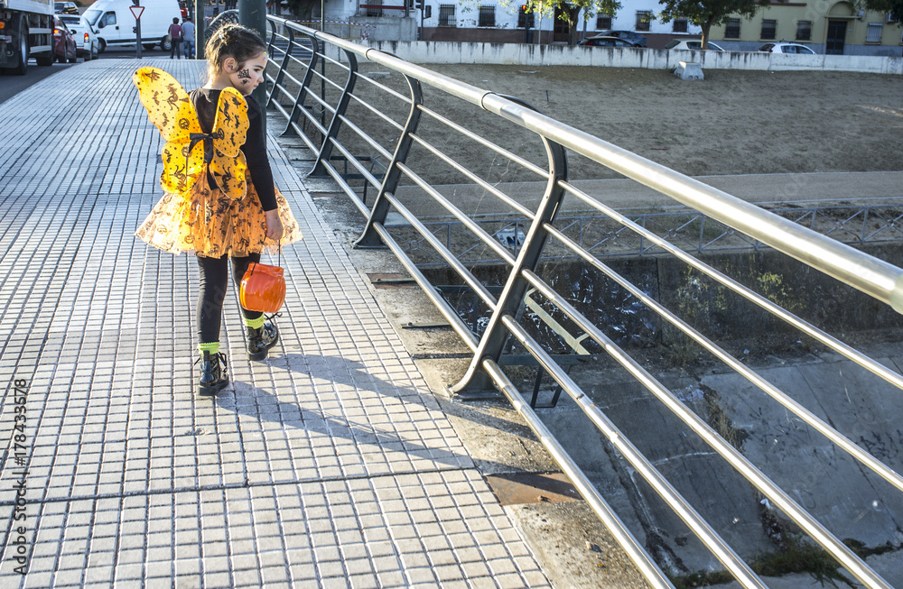 Little girl crossing urban bridge in halloween costumes towards children party site