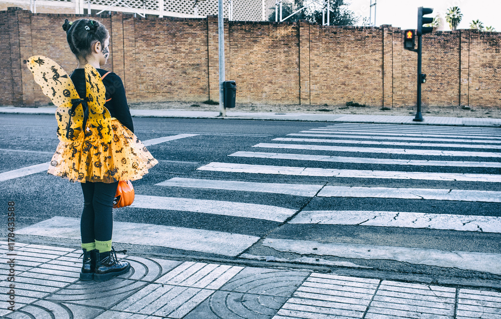 Fototapeta premium Little girl at zebra crossing in halloween costumes towards children party site