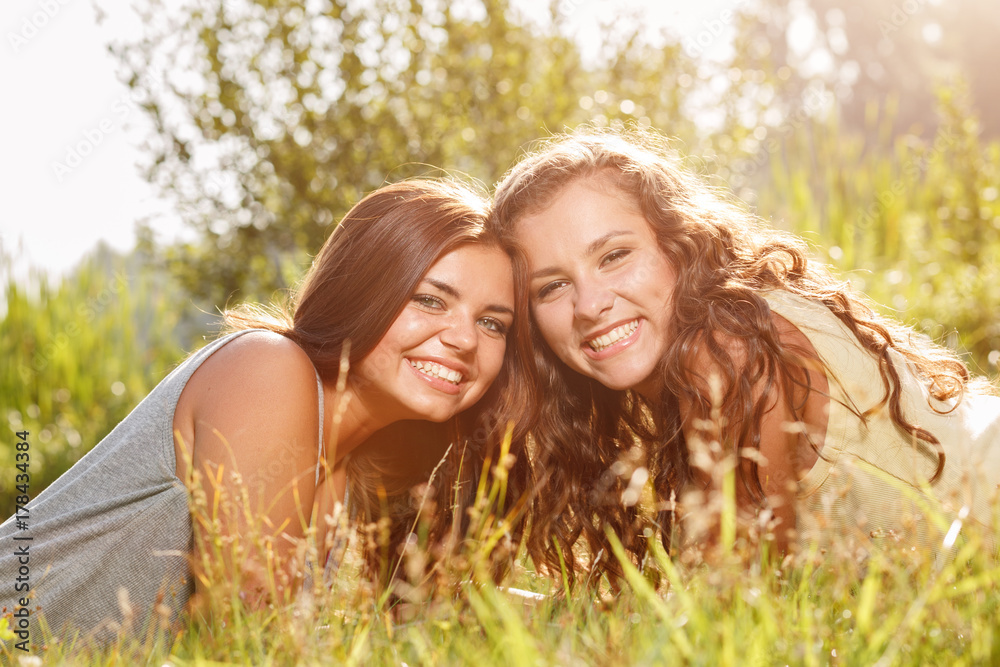 two young women lying down on green grass smiling happy two young women lying down on green grass smiling happy