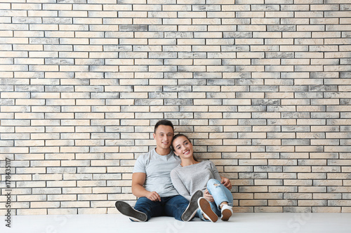 Happy young couple sitting on floor near brick wall in their new apartment. Moving house concept © Africa Studio