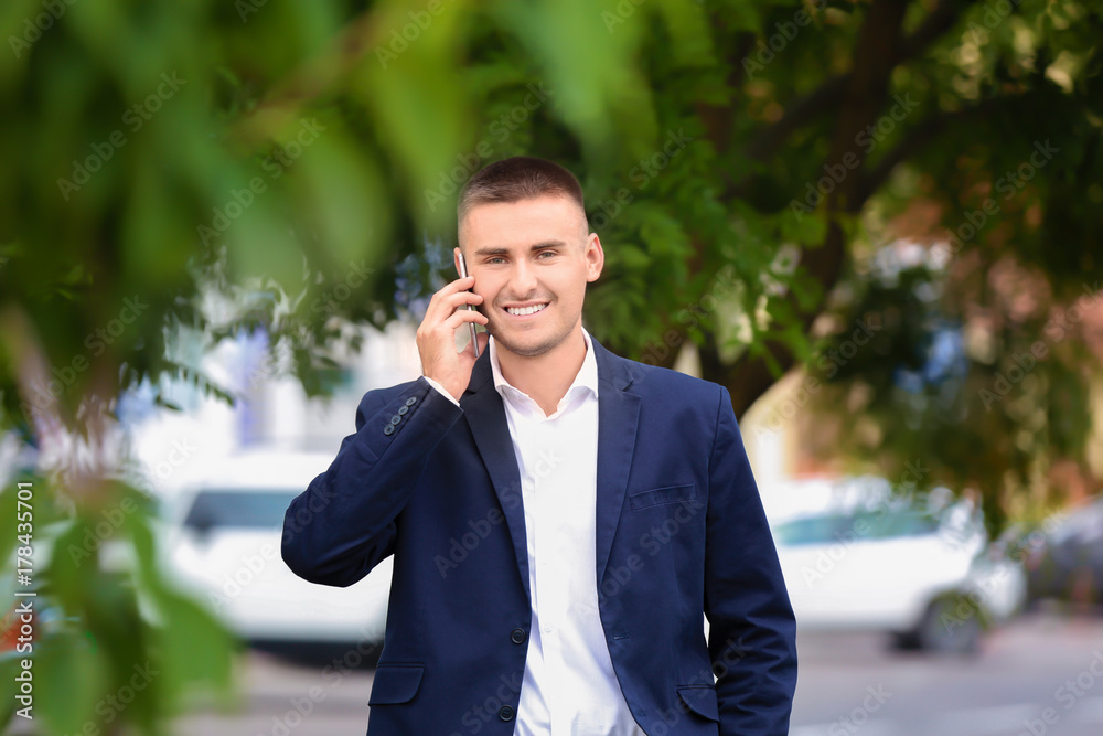 Handsome young businessman talking on mobile phone while walking in park Handsome young businessman talking on mobile phone while walking in park